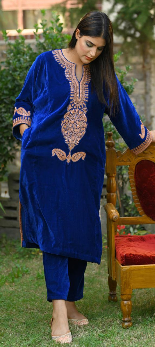 Woman wearing a blue embroidered traditional outfit standing outdoors.